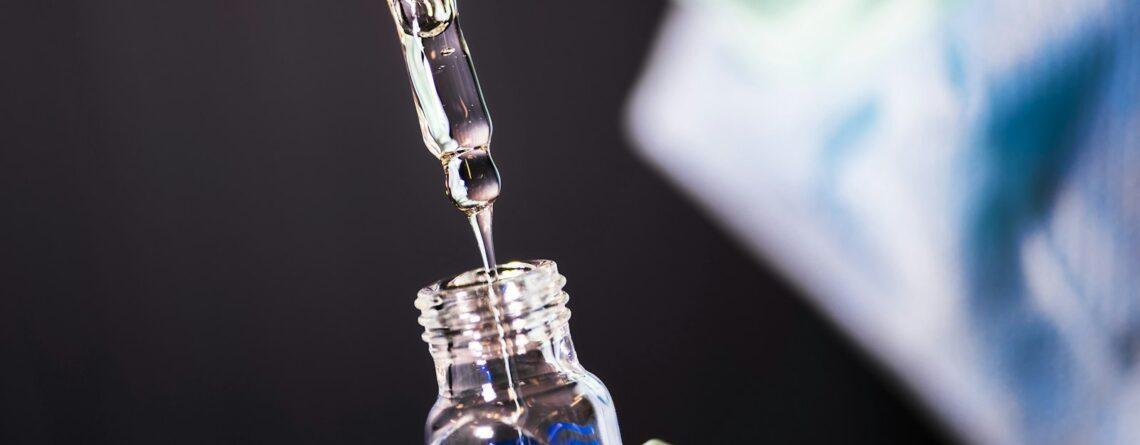 Gloved hand dripping liquid from a glass pipette into a vial